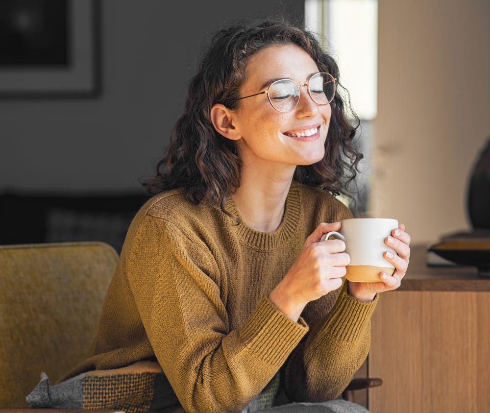 Woman with beautifully straight and white teeth smiling with eyes closed, holding a hot drink.