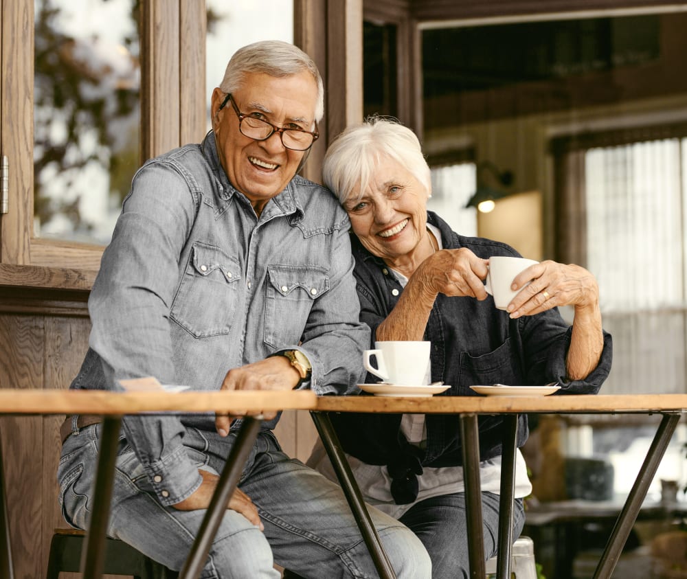Senior couple smiling for the camera as they enjoy a hot drink at a cafe together. 