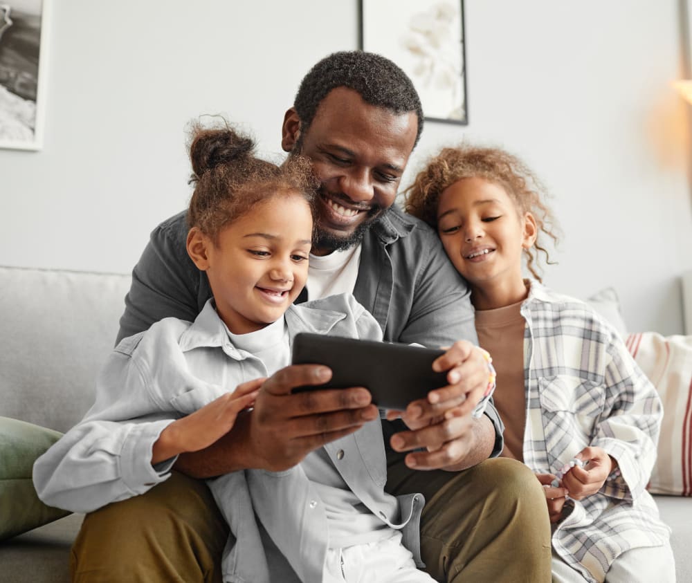 A father with two young daughters smiling as they enjoy looking at something on a phone together.