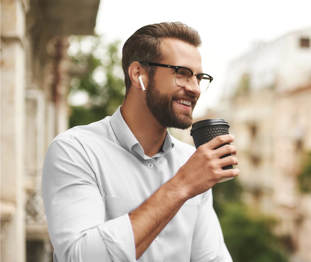 Man with glasses and a healthy looking smile, out on a balcony having a coffee. 