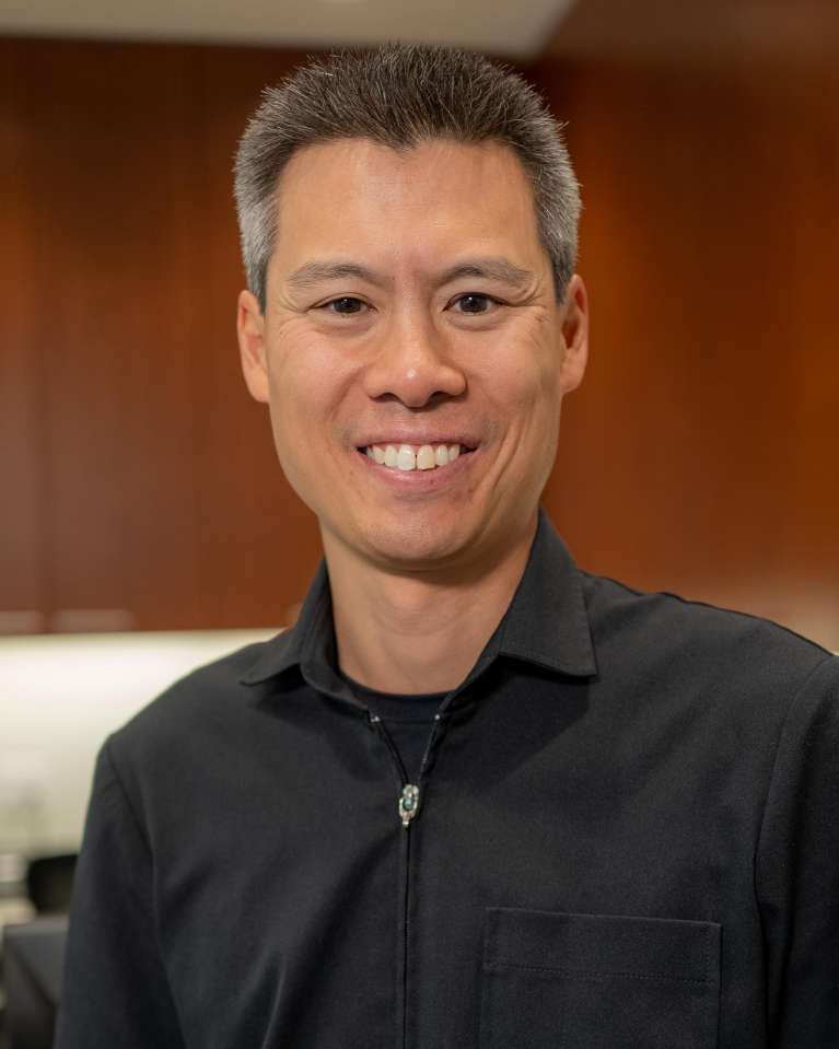 Portrait of our dentist Dr. Stephen King wearing a back shirt and smiling into the camera. smiling.