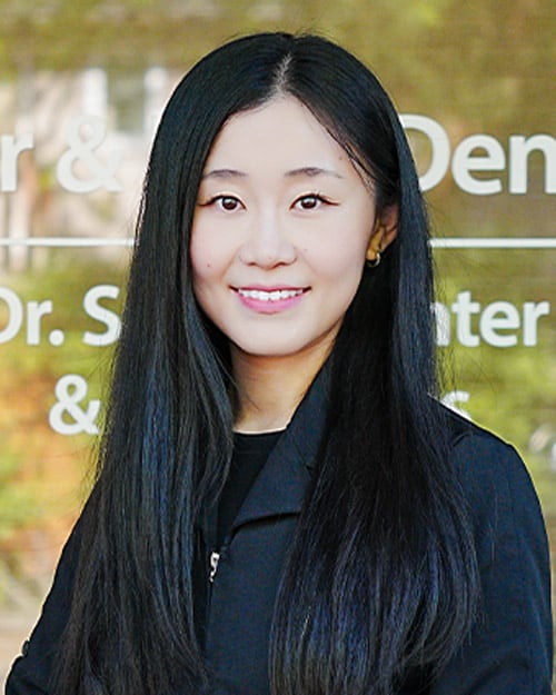 Portrait of our dentist Dr. Cindy Wei wearing a back shirt and smiling into the camera. smiling.